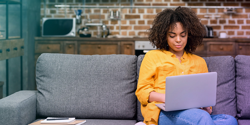 Young Black woman on couch with laptop