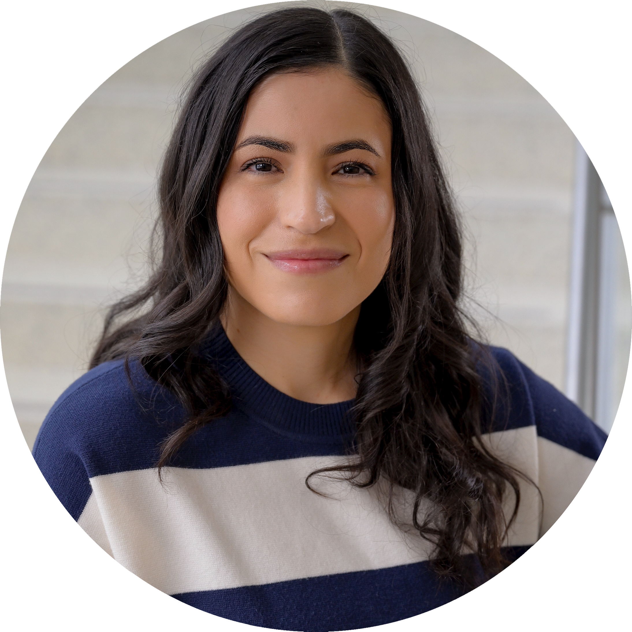 A headshot of Jennifer Vega with long dark hair in a navy and white striped sweater, smiling softly in front of a light-colored staircase