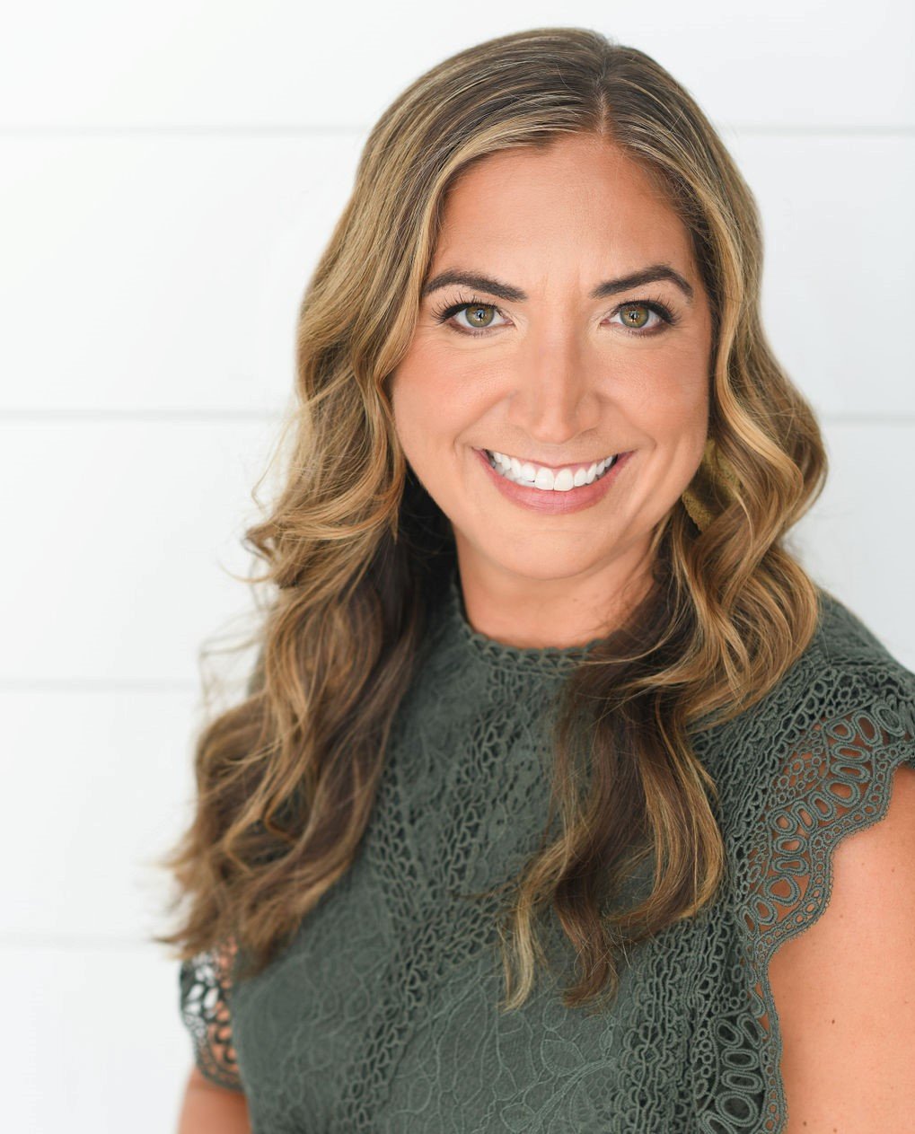 White woman with long blond hair and brown eyes wearing a green shirt smiling