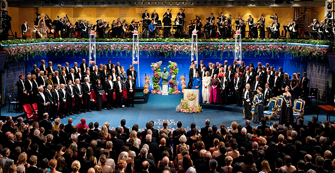 Stage with Nobel laureates, orchestra above, crowd below