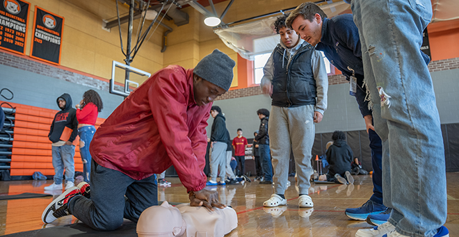 Scene in a gymnasium where a person is learning CPR on a manikin